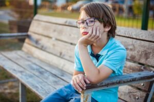 Sad, tired child sitting alone on the bench outdoors